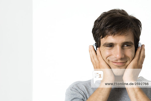 Man listening to headphones with hands over ears  smiling