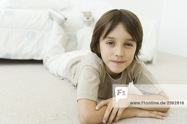 Junge liegt auf dem Boden im Schlafzimmer und lächelt in die Kamera.