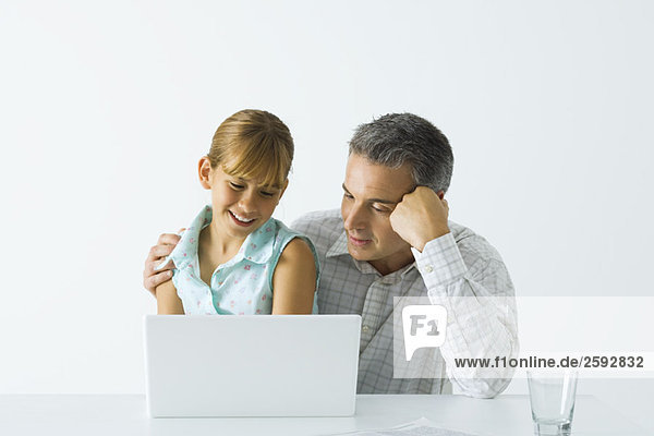 Vater und Tochter schauen zusammen auf Laptop-Computer  beide lächelnd