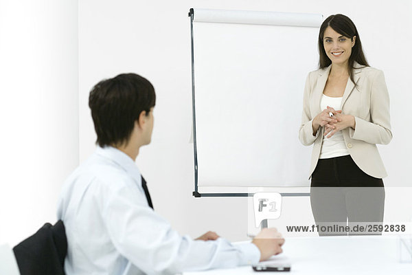 Geschäftsfrau bei der Präsentation  lächelnd vor der Kamera  männliche Kollegin beim Notieren