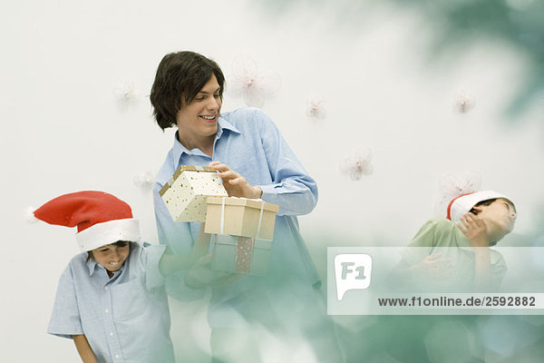 Junger Mann mit Geschenken  der mit zwei Jungen mit Weihnachtsmützen spielt.