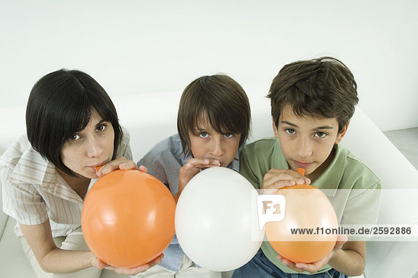 Mutter und zwei Söhne beim Aufblasen von Luftballons,  Blick in die Kamera,  Hochwinkelansicht