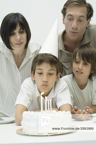 Familie sieht zu  wie der Junge Kerzen auf dem Geburtstagskuchen ausbläst.