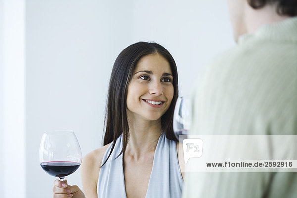 Frau hält ein Glas Rotwein und lächelt den Mann an  Blick in den Ausschnitt