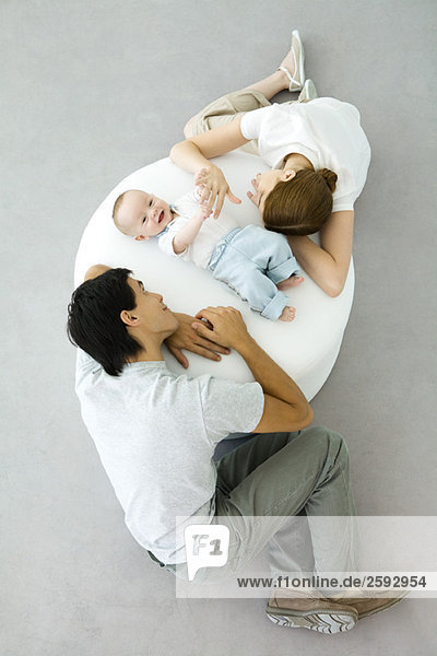 Eltern und Baby entspannen sich auf dem Hocker  Baby hält die Hand der Mutter  Blick nach oben