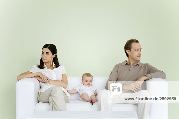 Couple sitting on couch with baby between them  both looking away