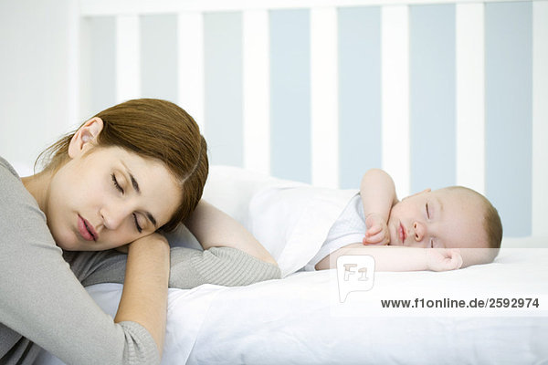 Mother resting head beside sleeping infant  eyes closed