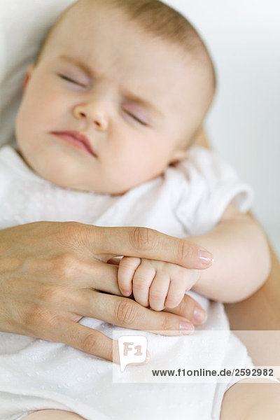 Baby schläft  hält den Finger der Mutter  Schnittansicht