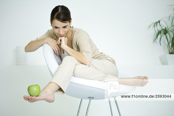 Frau sitzt im Stuhl und balanciert den Apfel zu Fuß.