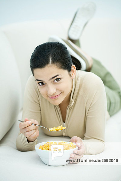 Young woman lying on stomach  eating bowl of cereal