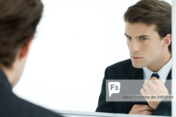 Businessman looking at self in mirror  adjusting tie