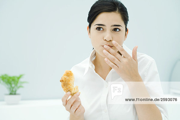 Junge Frau hält Croissant  andere Hand vor dem Mund