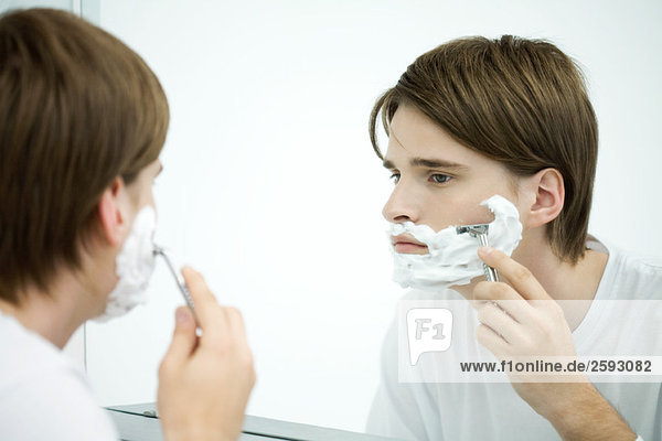 Junger Mann schaut sich im Spiegel an  rasiert sich.