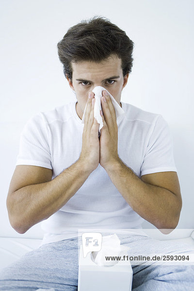 Man blowing his nose with a tissue  looking at camera
