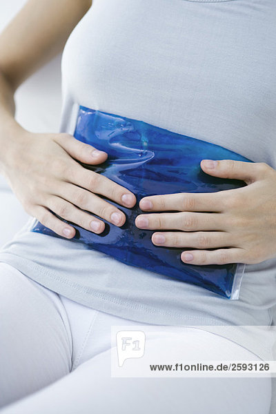 Woman holding ice pack against her stomach  cropped view