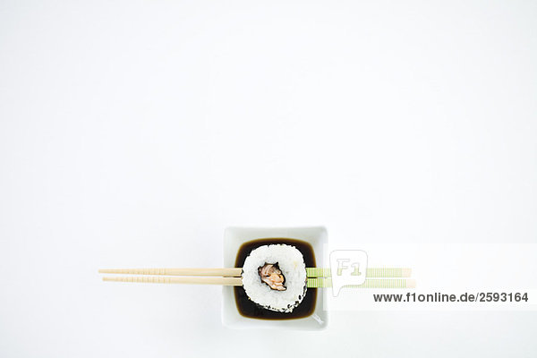 Einzelstück Maki-Sushi auf Essstäbchen über Sojasauce  Ansicht über Kopf