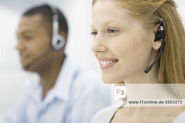 Woman wearing headset  male colleague in background  both working  smiling