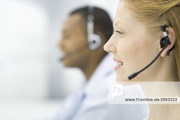 Close-up profile of woman wearing headset  male colleague in background