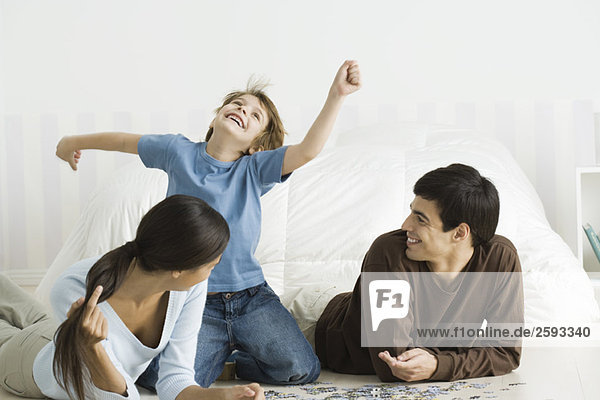 Family playing with jigsaw puzzle in bedroom  boy laughing  arms raised