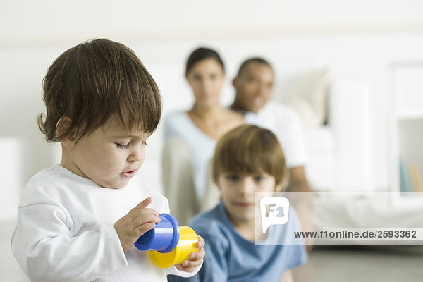 Kleinkind Mädchen spielt mit Spielzeug  Familie beobachtet im Hintergrund