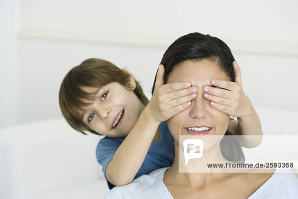 Little boy covering his mother's eyes with his hands  smiling at camera