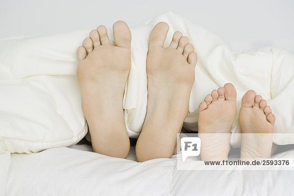 Parent and child's bare feet sticking out from under comforter  close-up