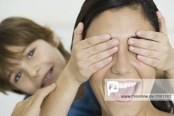 Boy covering mother's eyes with his hands  woman laughing