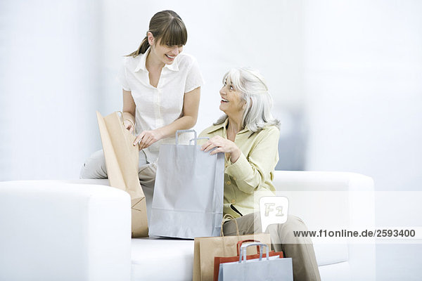 Seniorin und junge erwachsene Frau halten Einkaufstaschen und lächeln sich an.