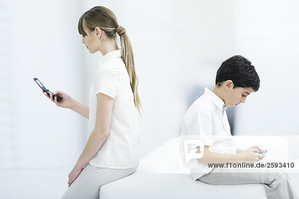 Junge Frau hält Handy mit eingeschaltetem Rücken Junge spielt Handheld-Videospiel