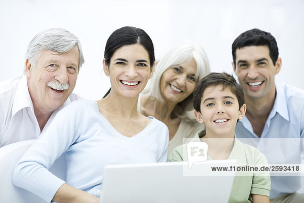 Multi-generation family gathered around laptop computer  smiling at camera