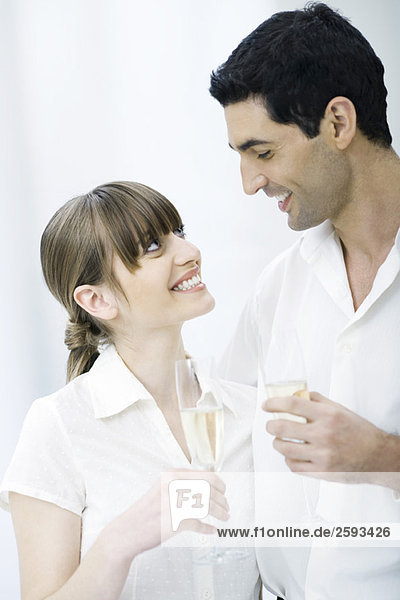 Ein Paar hält Gläser Champagner und lächelt sich an.