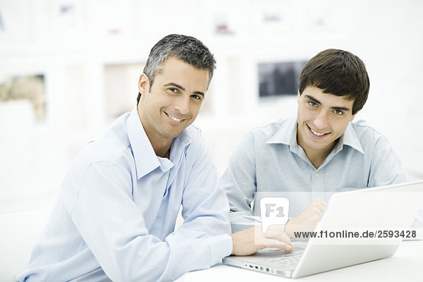 Two men using laptop computer together  both smiling at camera