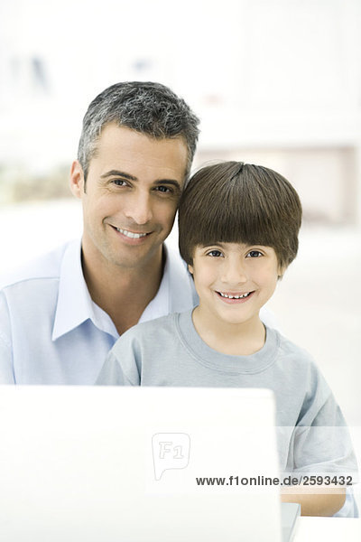 Father and son sitting with laptop computer  smiling  portrait