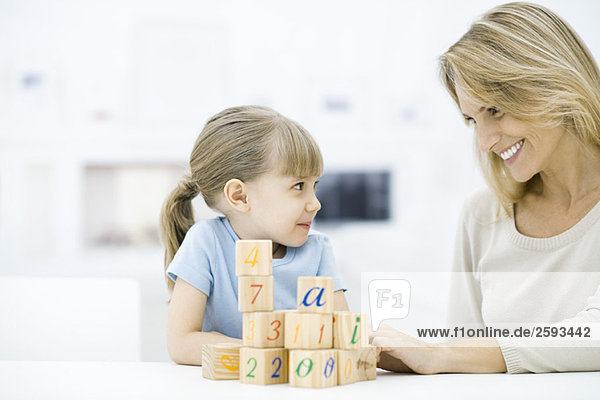 Mother and daughter sitting with blocks  smiling at each other
