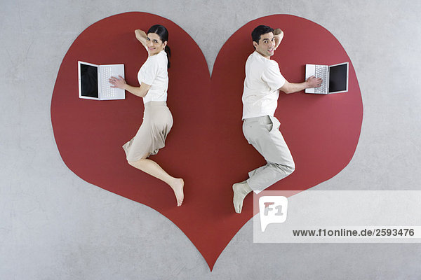 Mann und Frau liegen auf großer Herzgrafik  beide mit Laptop-Computer