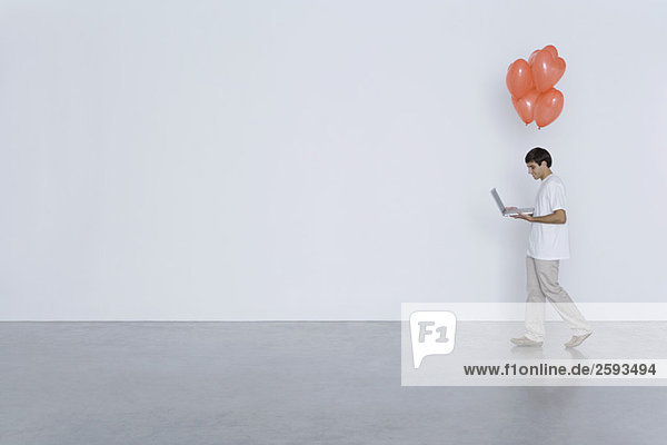 Man carrying laptop computer and heart balloons  side view