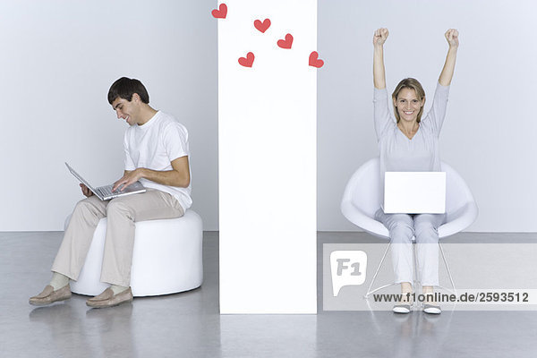 Mann und Frau benutzen Laptops  Herzen schweben zwischen ihnen  die Arme der Frau erhoben.