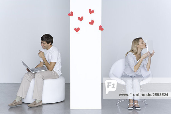 Woman kissing laptop computer  man looking at his own laptop and smiling  hearts in the air between them