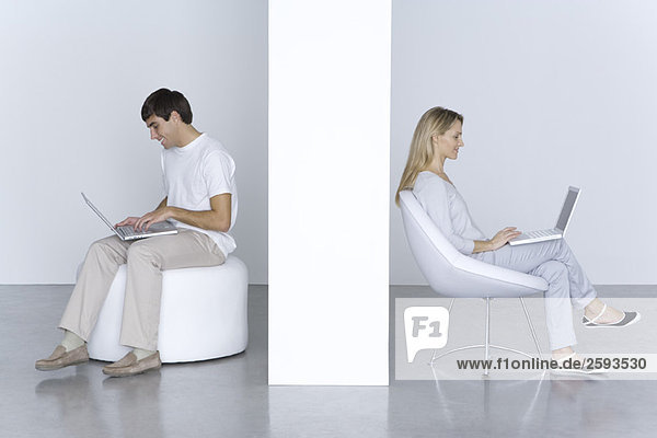 Man and woman sitting separately  using laptop computers  smiling