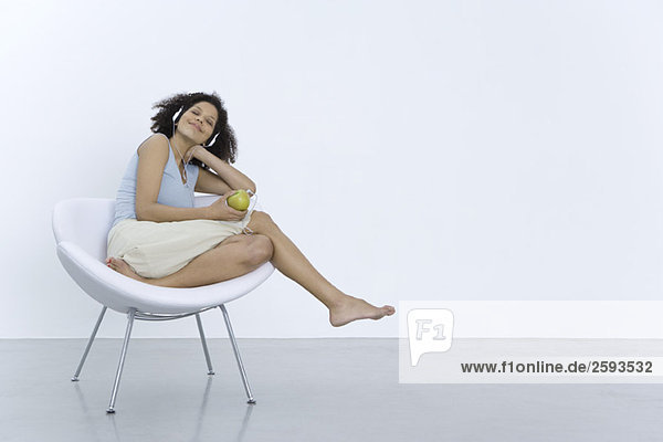 Woman sitting in chair  listening to headphones connected to apple  smiling