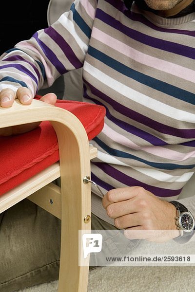 Ein Mann  der einen Inbusschlüssel benutzt  um eine Schraube an einem Stuhl festzuziehen.