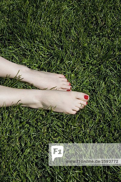 Eine junge Frau mit nackten Füßen und rot lackierten Zehennägeln auf Gras.