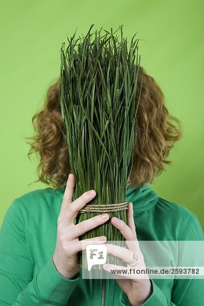 Eine Frau hält ein gebundenes Bündel geschnittenes Gras vor ihr Gesicht.