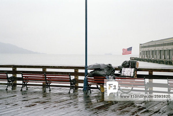 A person sitting on a bench in the rain  overlooking San Francisco Bay  USA