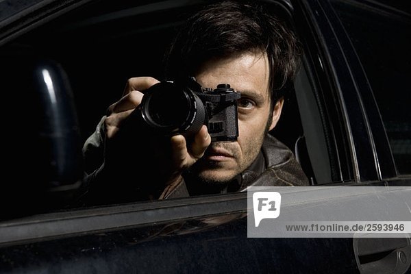 Ein Mann  der mit einer Kamera von seinem Auto aus überwacht.