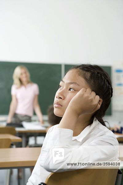 A pre-adolescent girl sitting in the back of a classroom looking bored