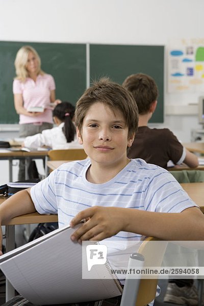 A pre-adolescent boy sitting in the back of a classroom  looking at camera