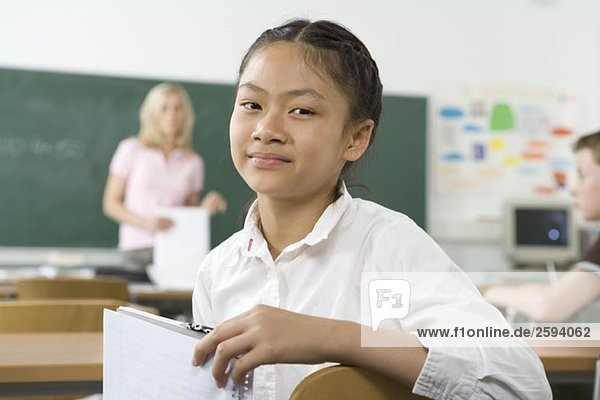 A pre-adolescent girl sitting in the back of a classroom  looking at camera
