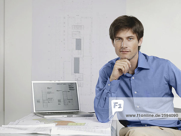 An architect sitting at his desk with a laptop and architectural drawings