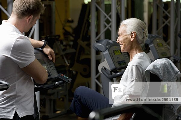 A senior woman on a stationary bike learning from an instructor